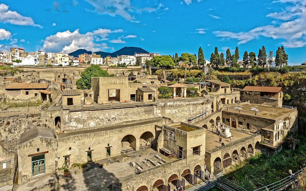 Panoramic view of ancient ruins in Herculaneum, Italy, with Mount Vesuvius in the background.