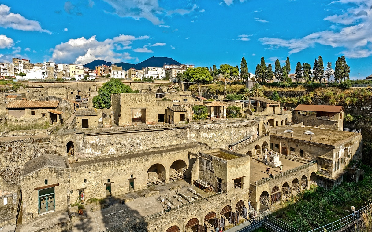 Panoramic view of ancient ruins in Herculaneum, Italy, with Mount Vesuvius in the background.
