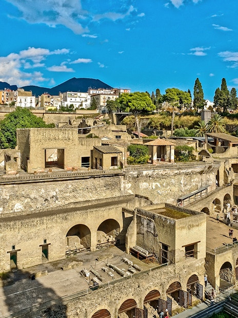 Panoramic view of ancient ruins in Herculaneum, Italy, with Mount Vesuvius in the background.