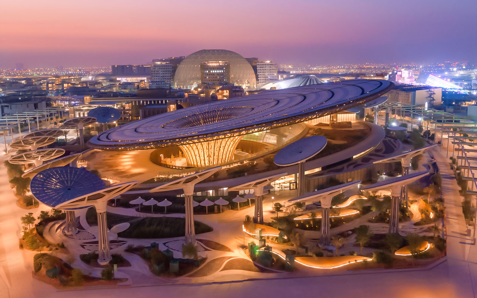 Exterior view of Expo City Dubai at sunset, featuring futuristic architecture and illuminated pathways.