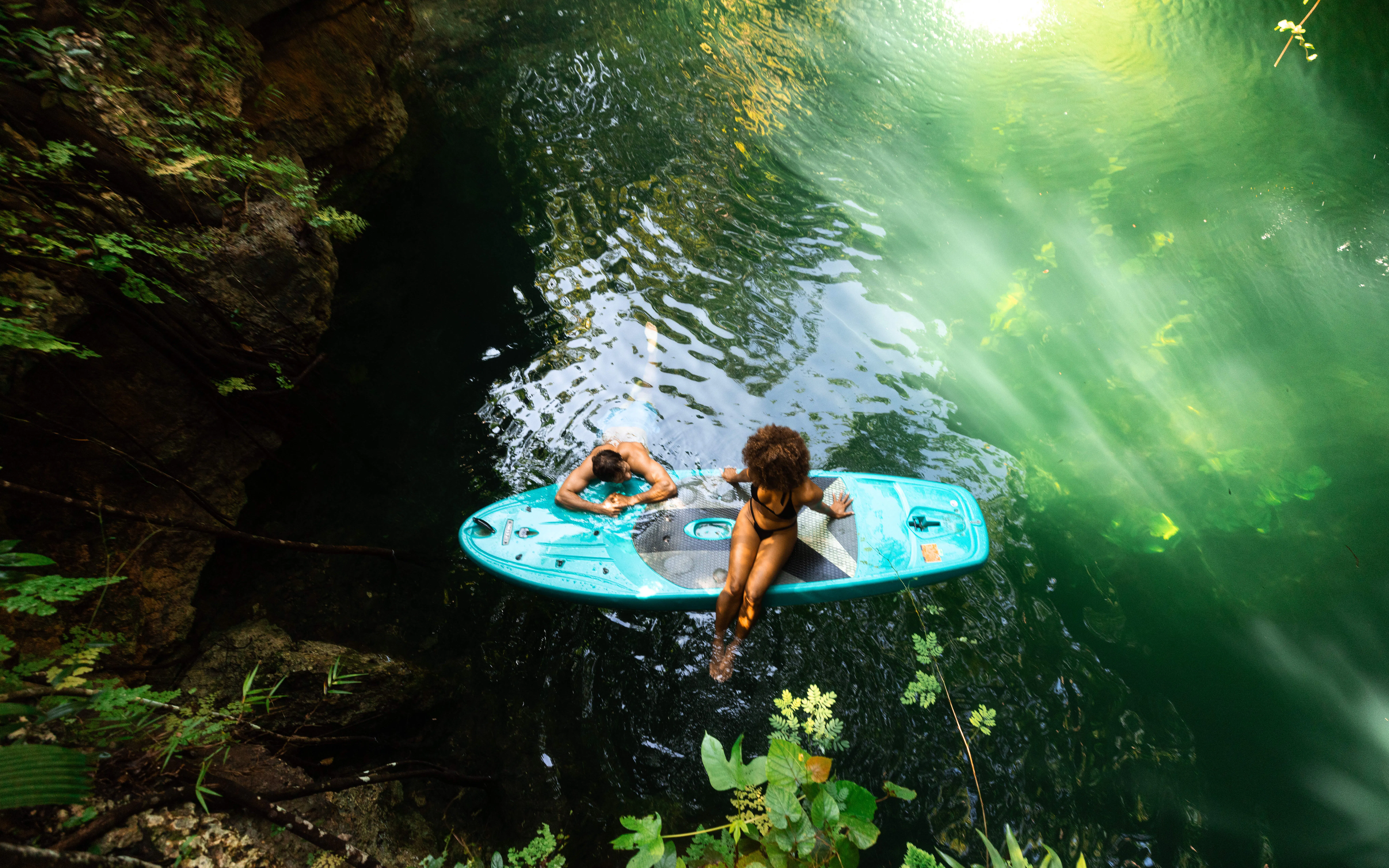 Couple relaxing on a paddleboard in a cenote surrounded by lush greenery.