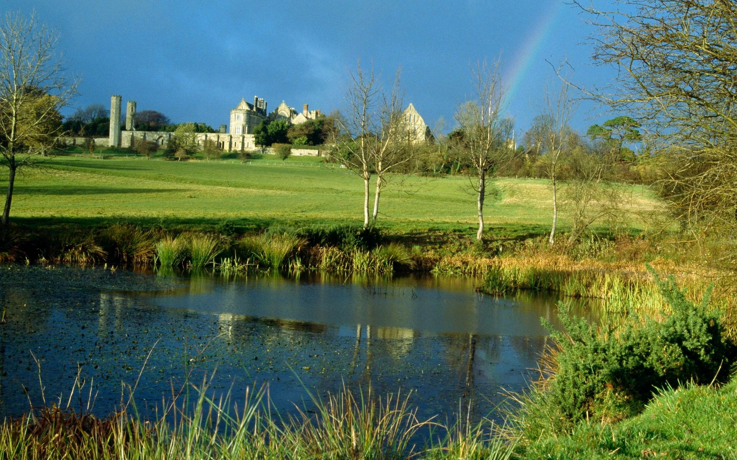 Battle Abbey ruins with surrounding landscape and pond in East Sussex, England.