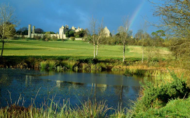 Battle Abbey ruins with surrounding landscape and pond in East Sussex, England.