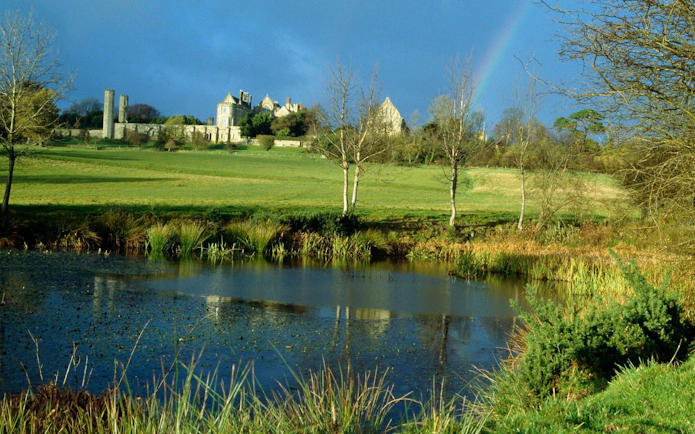 Battle Abbey ruins with surrounding landscape and pond in East Sussex, England.