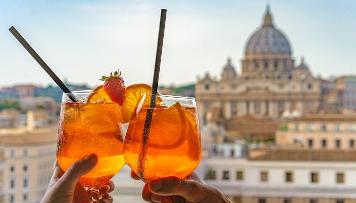 Tourist holding prosecco spritz with St Peter's Basilica in the background, Rome.