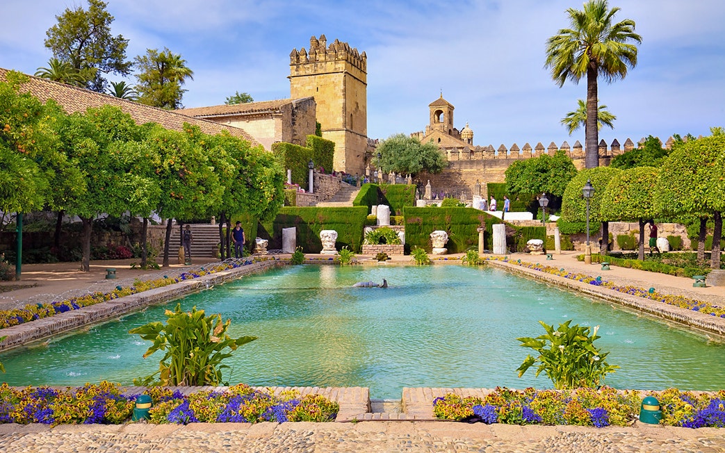 Córdoba Alcázar gardens with pool and historic tower in background.