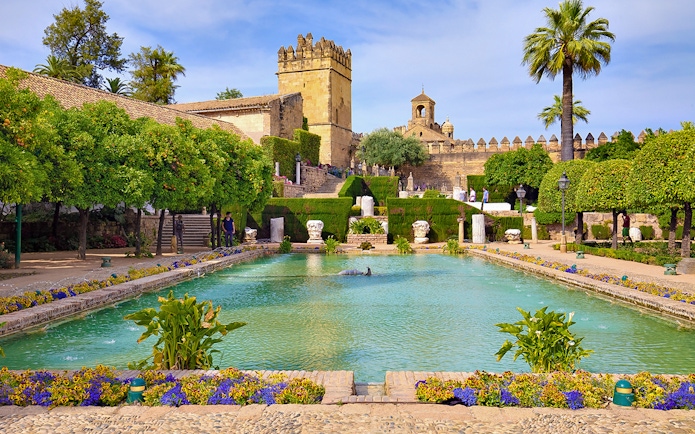 Córdoba Alcázar gardens with pool and historic tower in background.