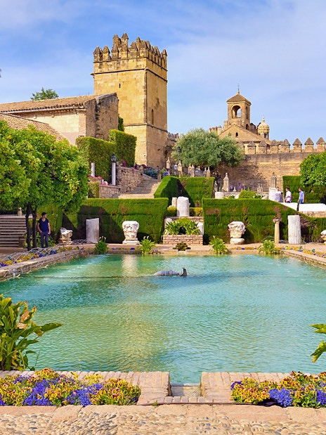 Córdoba Alcázar gardens with pool and historic tower in background.