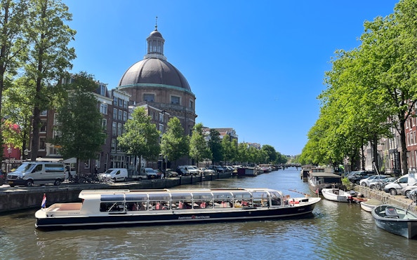 Canal boat cruising past the dome of St. Nicholas Church in Amsterdam.