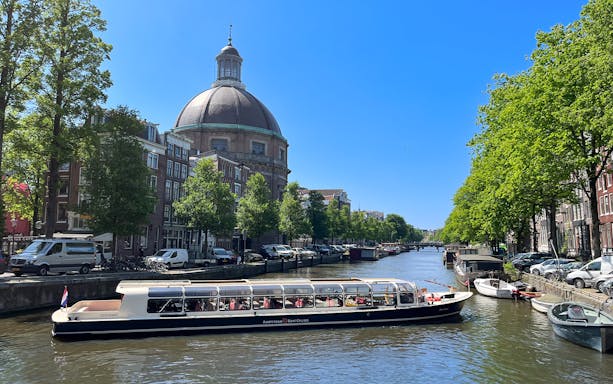 Canal boat cruising past the dome of St. Nicholas Church in Amsterdam.