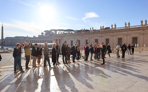 St. Peter’s Basilica interior with ornate ceiling and visitors on a guided tour in Vatican City.