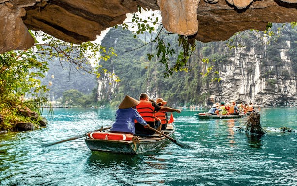 Boat tour through limestone caves in Tam Coc, Vietnam, with tourists rowing on a serene river.