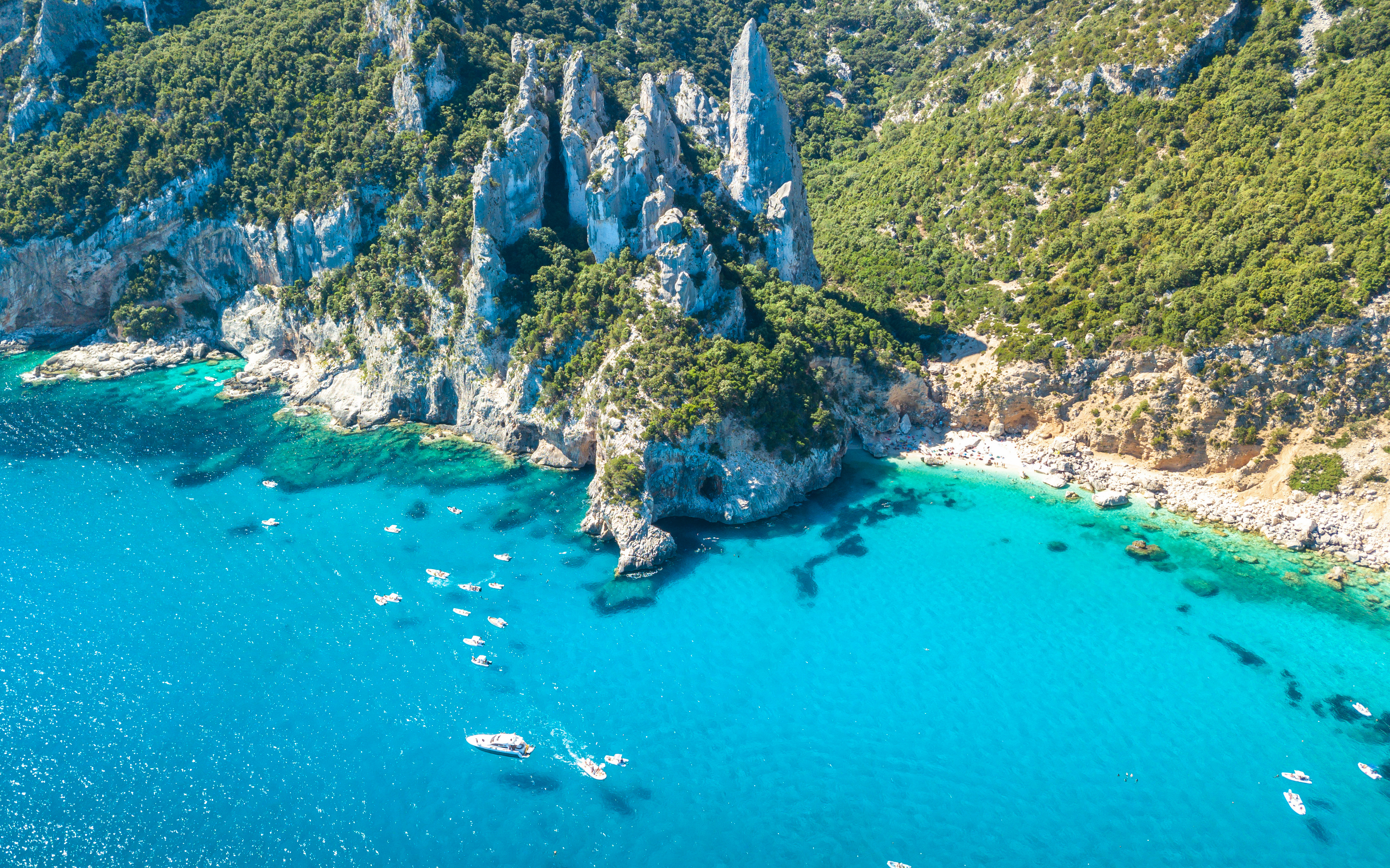 Boats in turquoise waters near rocky cliffs at Cala Goloritze, Gulf of Orosei, Sardinia, Italy.