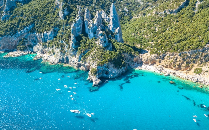 Boats in turquoise waters near rocky cliffs at Cala Goloritze, Gulf of Orosei, Sardinia, Italy.