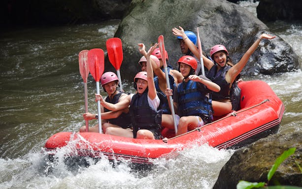 Group rafting on Ayung River in Bali, navigating rapids with paddles raised.