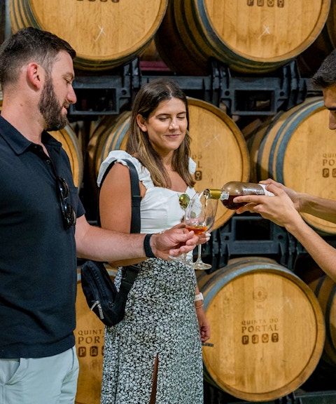 Tourist with guide tasting wine in a cellar with wooden barrels Douro