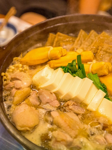 Sumo wrestlers hot pot with tofu, vegetables, and chicken in a steaming broth.