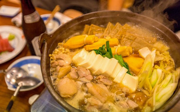 Sumo wrestlers hot pot with tofu, vegetables, and chicken in a steaming broth.