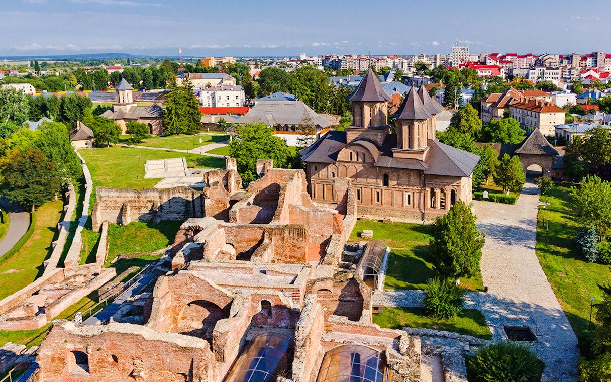 Old town ruins and church in Targoviste, Romania, with surrounding greenery and cityscape.