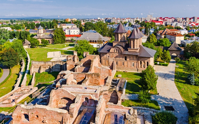 Old town ruins and church in Targoviste, Romania, with surrounding greenery and cityscape.