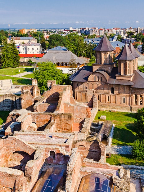 Old town ruins and church in Targoviste, Romania, with surrounding greenery and cityscape.