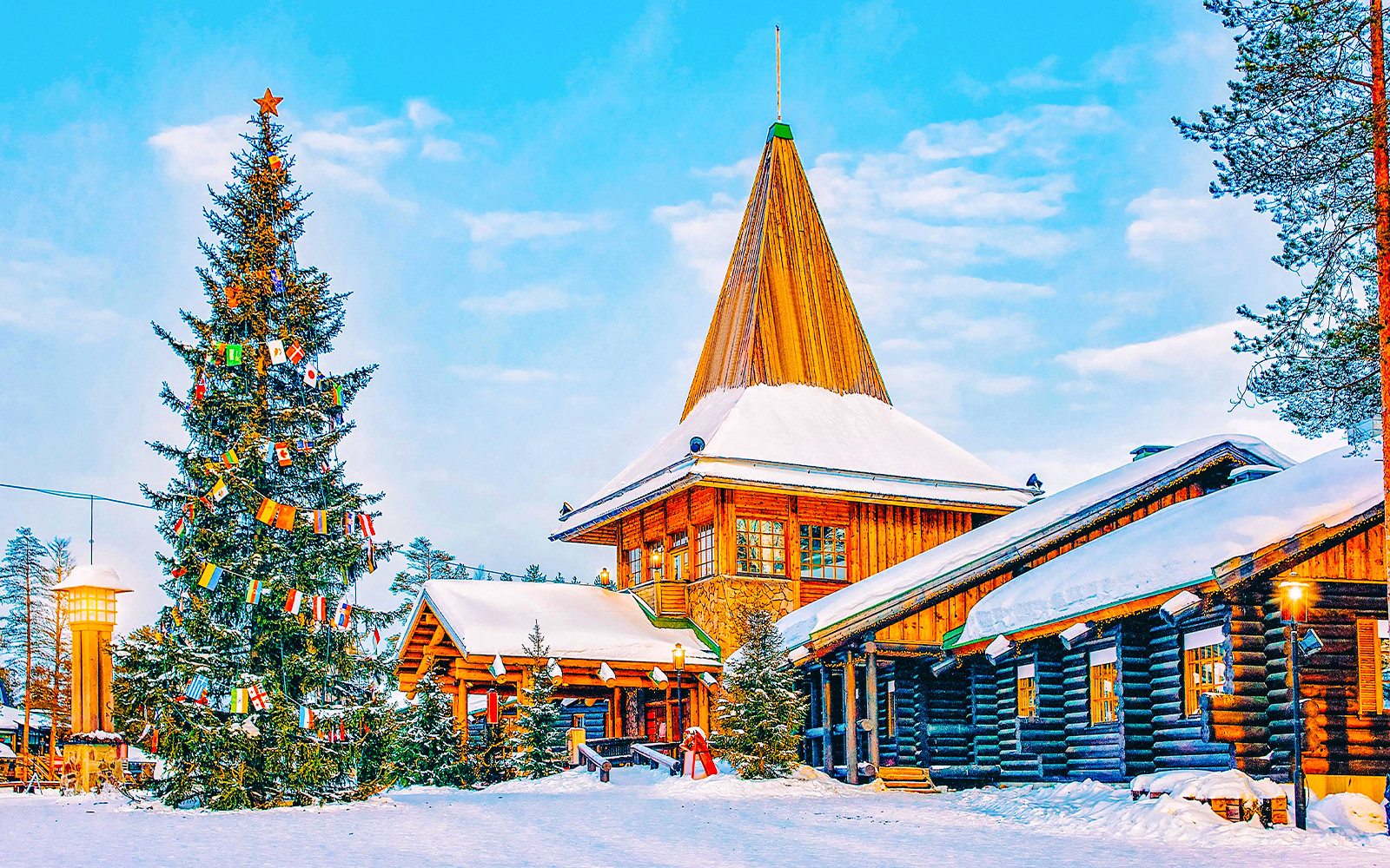 Santa Claus Village in Rovaniemi with snow-covered log buildings and decorated Christmas tree.