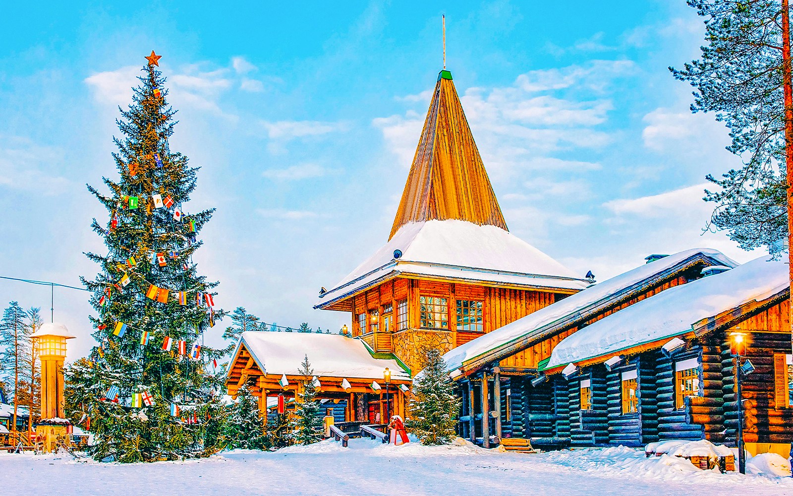 Santa Claus Village in Rovaniemi with snow-covered log buildings and decorated Christmas tree.
