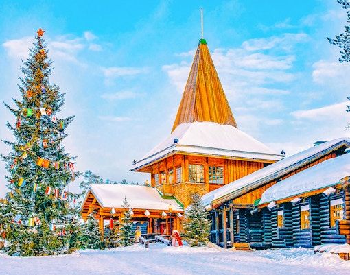 Santa Claus Village in Rovaniemi with snow-covered log buildings and decorated Christmas tree.