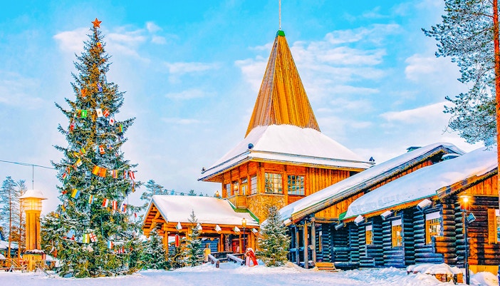 Santa Claus Village in Rovaniemi with snow-covered log buildings and decorated Christmas tree.