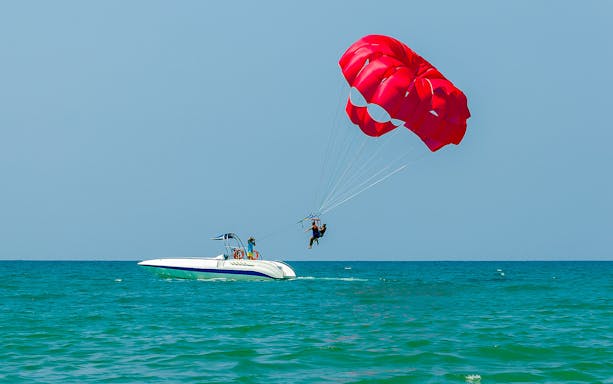 Parasailing over the ocean in Albufeira with a red parachute.