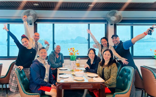 Group enjoying a meal at a table inside a cruise ship dining room with ocean view.