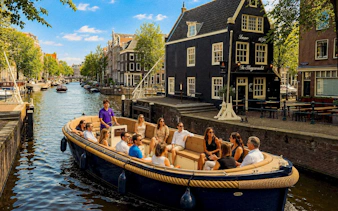 Open boat with tourists cruising Amsterdam canal in the morning.