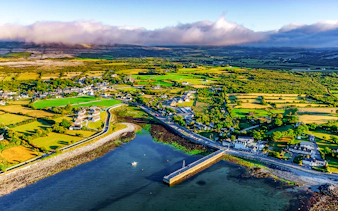 Aerial view of Ballyvaughan village and coastline, featuring lush fields and a small harbor.