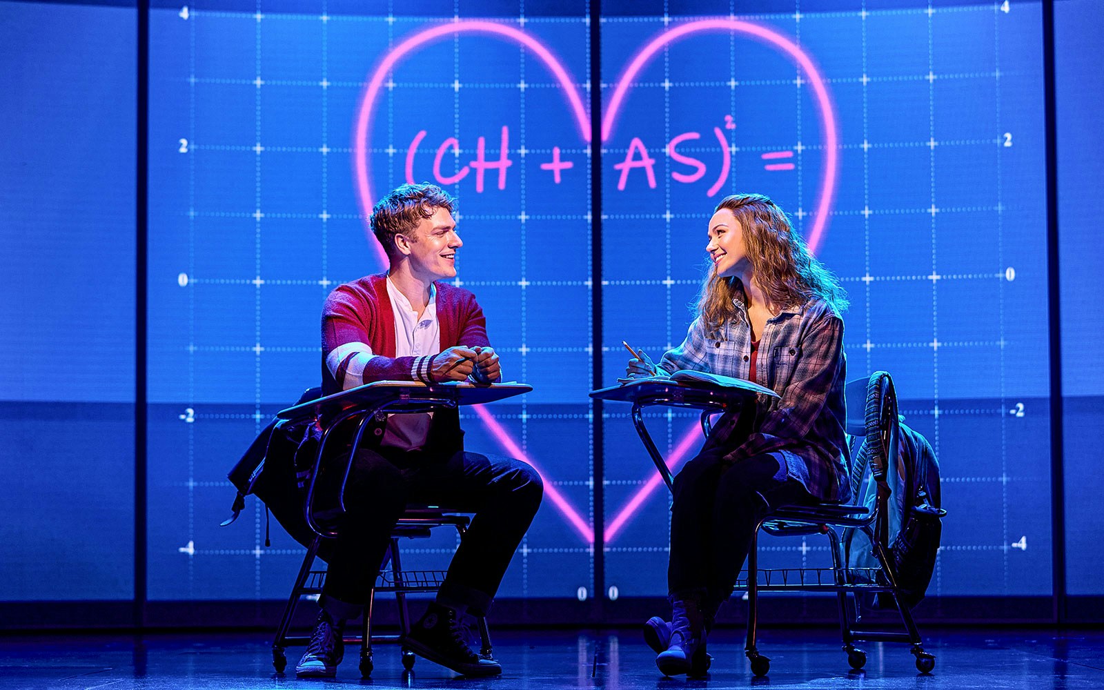 Two actors in a classroom scene from Mean Girls The Musical, with a heart equation on the board.