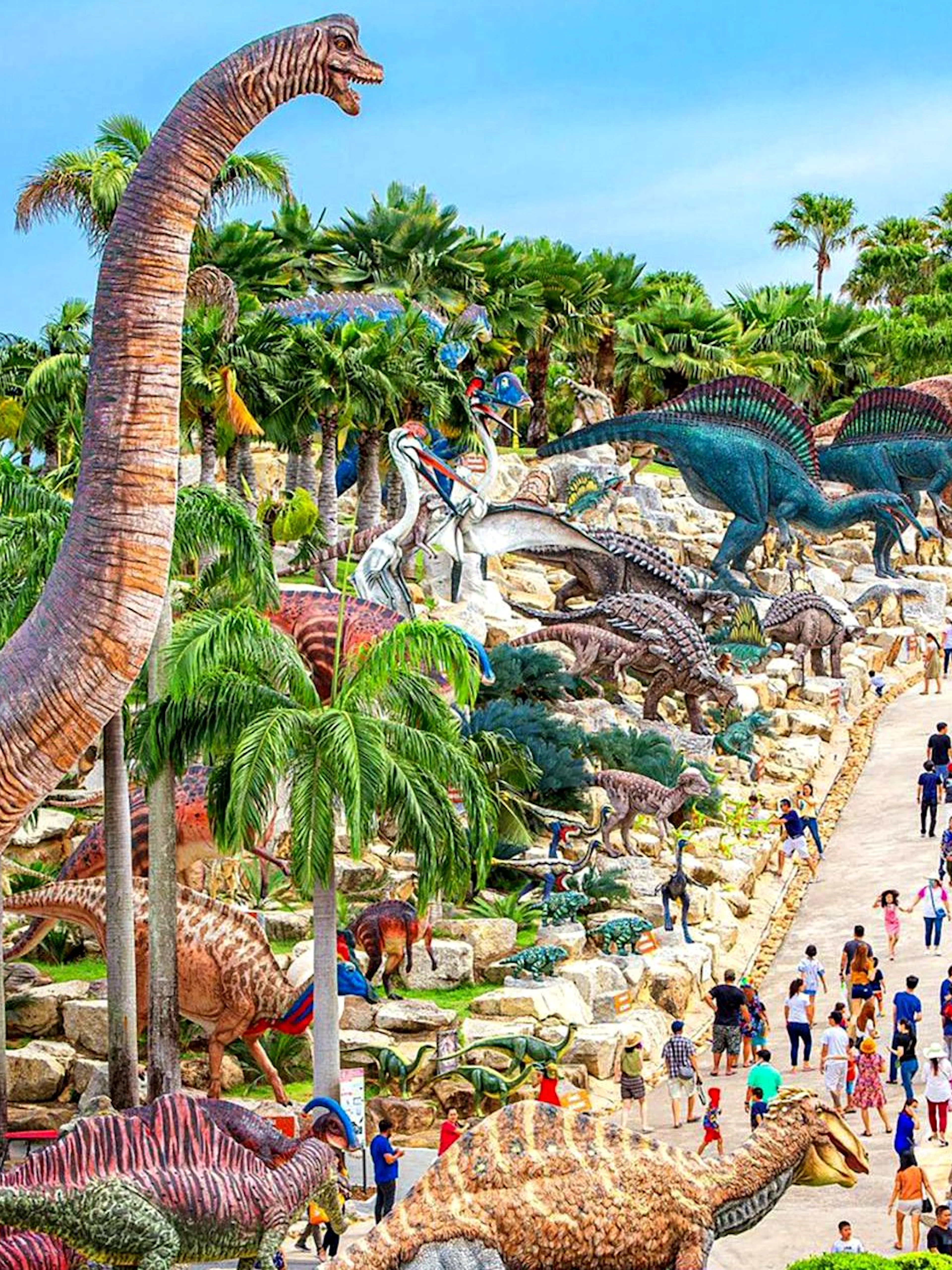 Nong Nooch Tropical Garden dinosaur sculptures and visitors on a pathway in Thailand.
