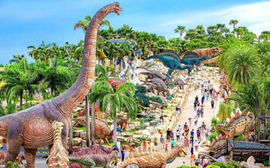 Nong Nooch Tropical Garden dinosaur sculptures and visitors on a pathway in Thailand.