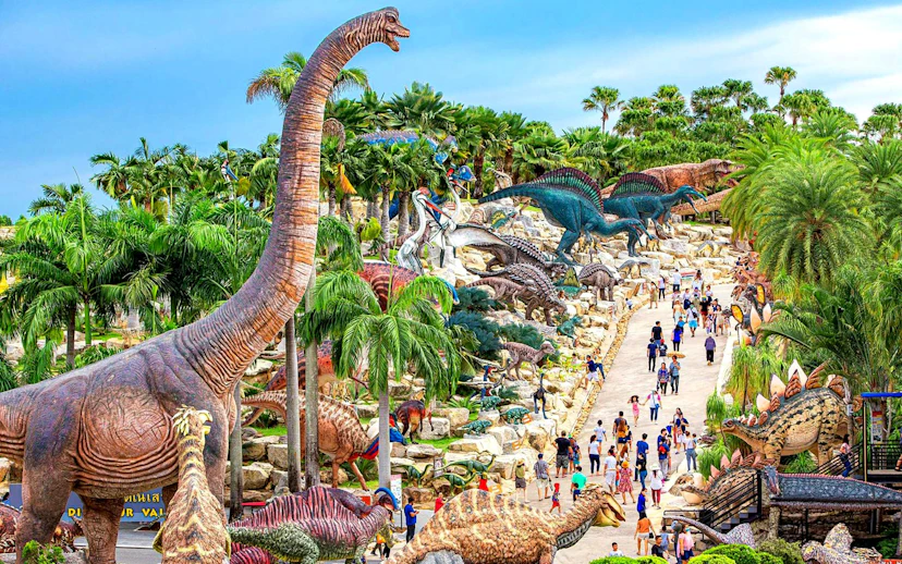 Nong Nooch Tropical Garden dinosaur sculptures and visitors on a pathway in Thailand.