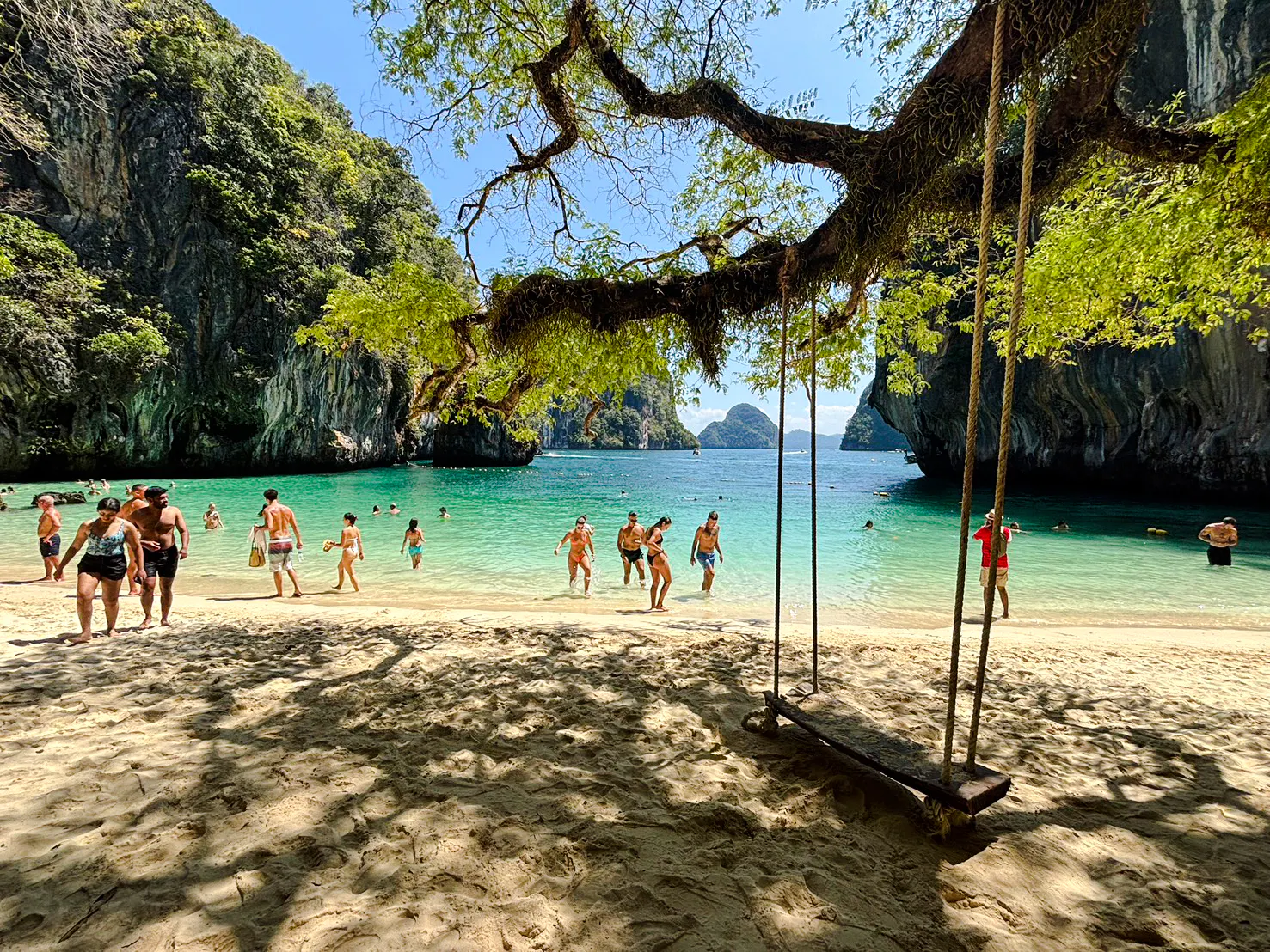 Tourists enjoying the beach and swimming at Hong Islands, Krabi, with a view of limestone cliffs.