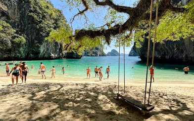Tourists enjoying the beach and swimming at Hong Islands, Krabi, with a view of limestone cliffs.