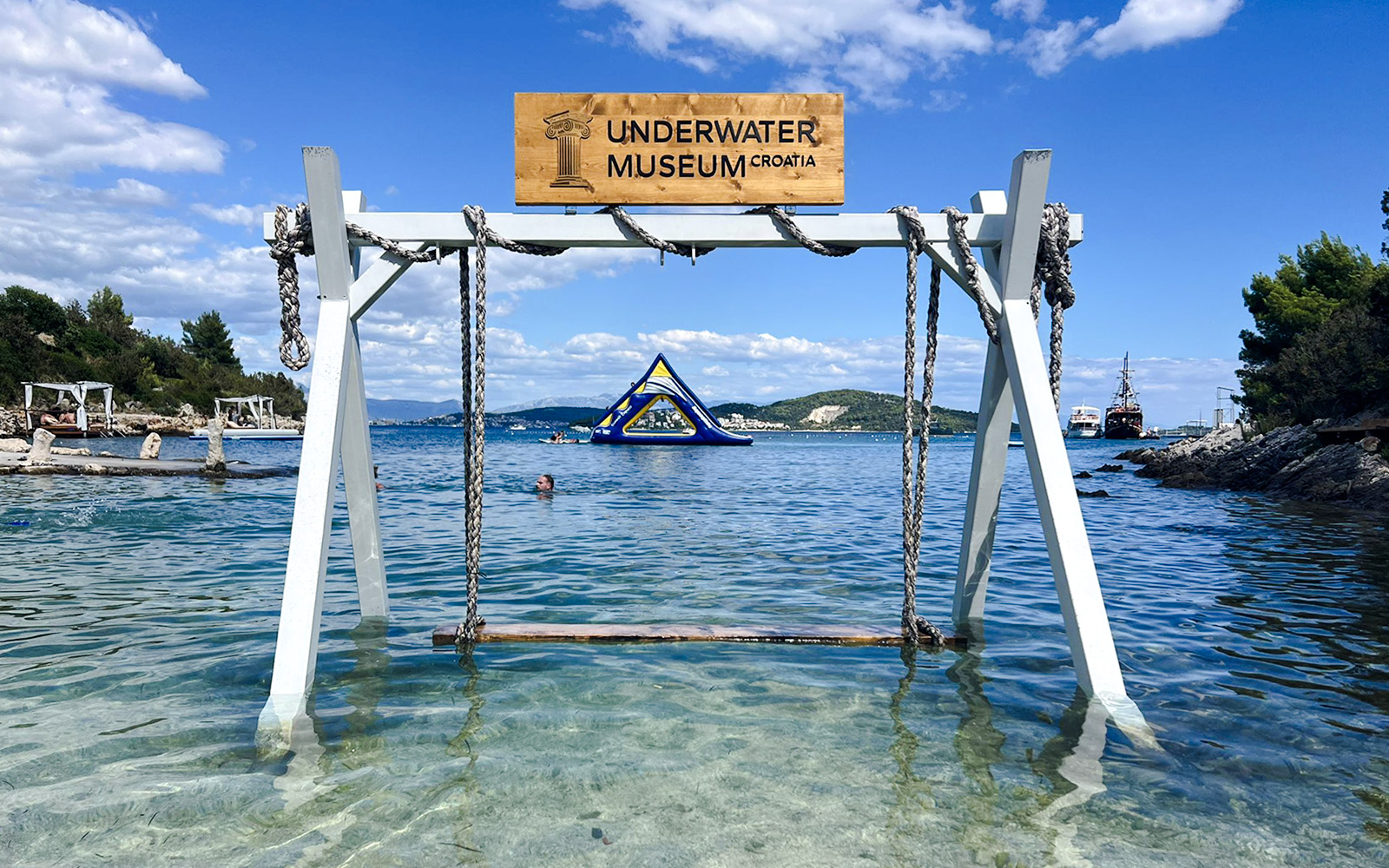 Underwater Museum sign at Blue Lagoon, Croatia with clear water and distant inflatable structure.