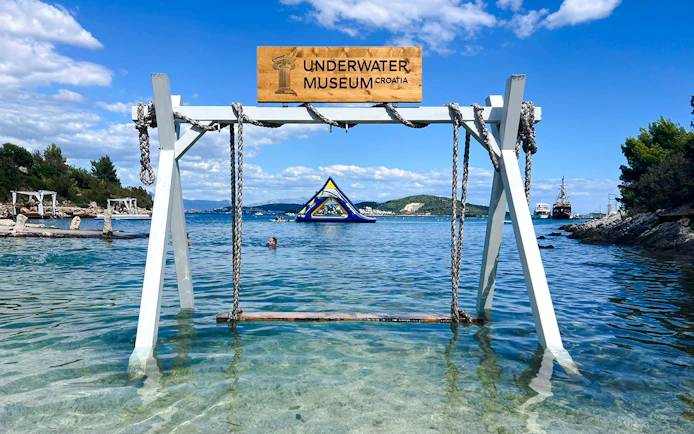 Underwater Museum sign at Blue Lagoon, Croatia with clear water and distant inflatable structure.