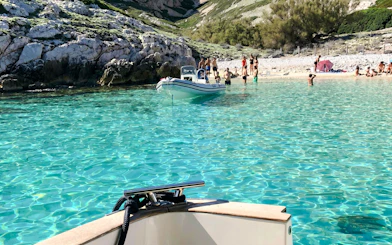 Boat approaching Frioul Archipelago beach with clear turquoise water and rocky shoreline.