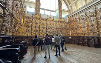 Tourists with guide inside Mosteiro de São Bento da Vitória, Porto, viewing ornate gold interior.