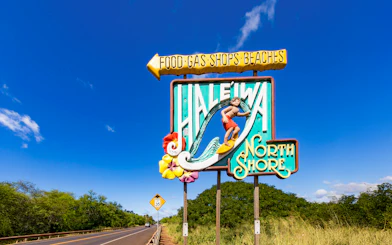 Haleiwa Town sign with surfer and North Shore text on a sunny day.