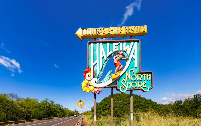 Haleiwa Town sign with surfer and North Shore text on a sunny day.