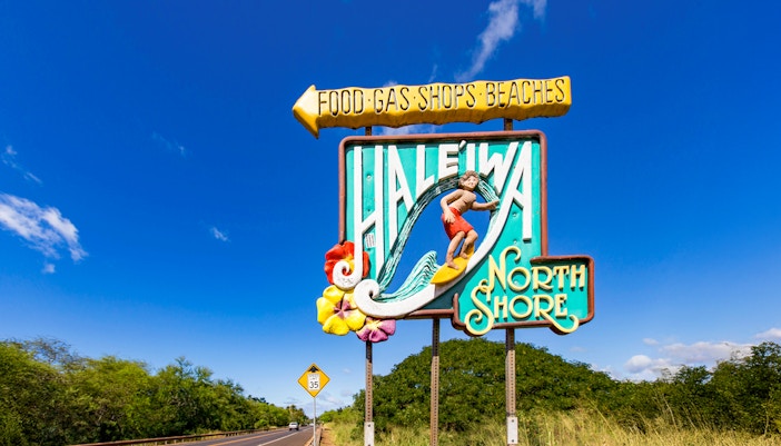Haleiwa Town sign with surfer and North Shore text on a sunny day.