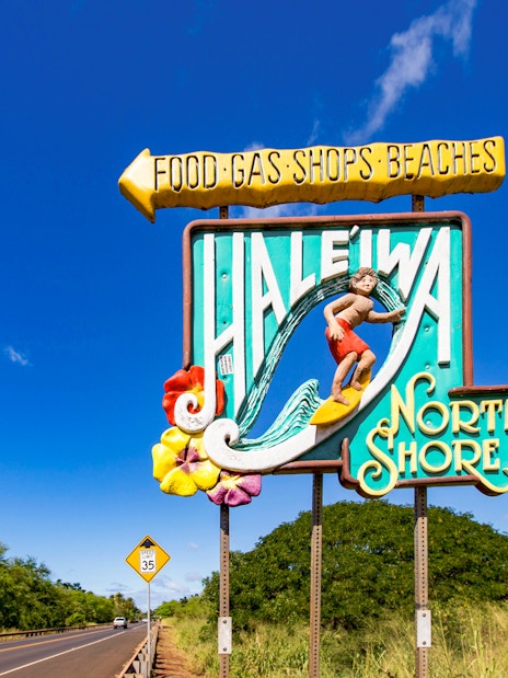 Haleiwa Town sign with surfer and North Shore text on a sunny day.
