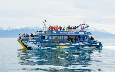 Whale watching boat with tourists in Kaikoura, New Zealand, snowy mountains in background.
