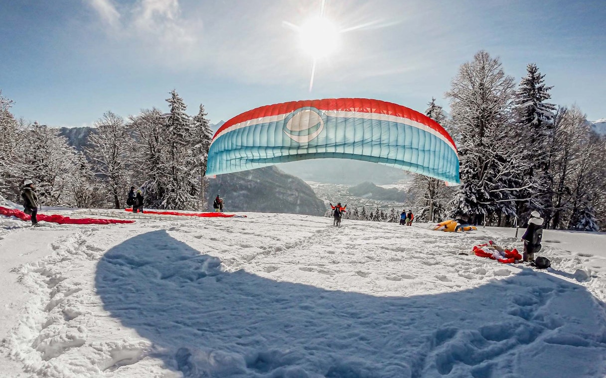 Paragliders preparing for takeoff on a snowy hill in Interlaken during winter.