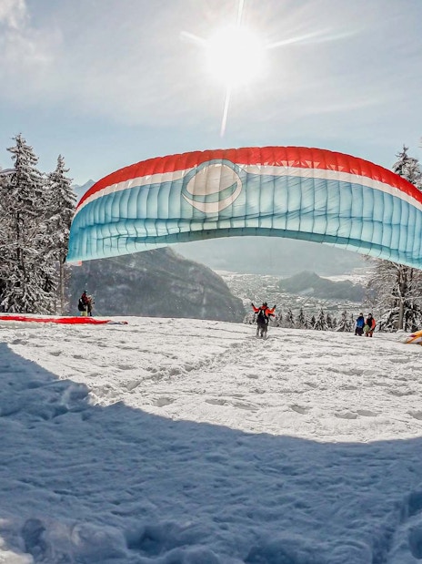Paragliders preparing for takeoff on a snowy hill in Interlaken during winter.
